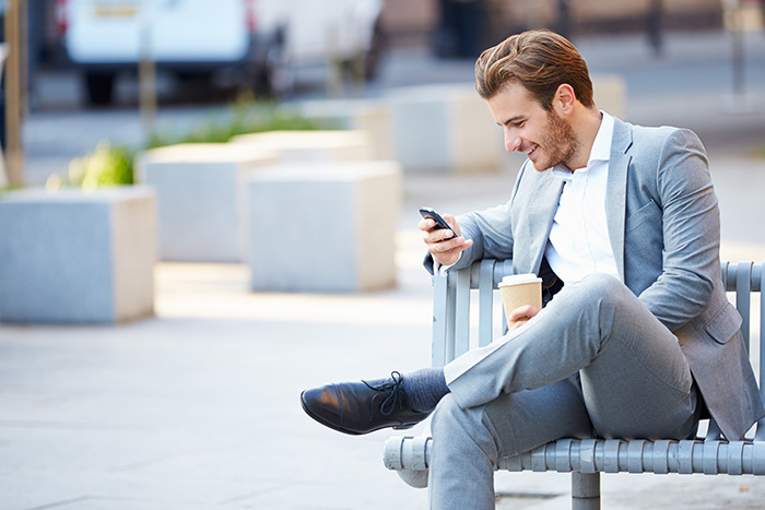 Businessman On Park Bench With Coffee Using Mobile Phone