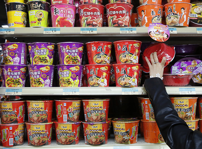 A woman chooses a cup noodle from a shelf displaying cup noodles from Uni-President China (top and middle) and Tingyi (bottom) at a supermarket in Beijing October 9, 2013. The price war for China's $8.8 billion instant noodle market sparked last year by Uni-President China Holdings Ltd's porcine giveaways soon escalated into free drinks, extra seasonings and other gifts as incumbent heavyweight Tingyi (Cayman Islands) Holdings Corp, owner of the Master Kong brand, sought to defend its patch. While Chinese consumers who slurp their way through 44 billion packets of noodles each year were delighted, shareholders were left underwhelmed.  REUTERS/Kim Kyung-Hoon (CHINA - Tags: FOOD BUSINESS) - RTX145BK
