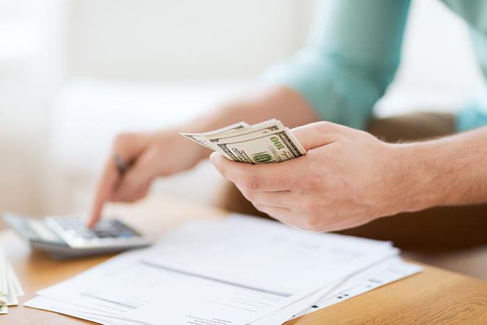 savings, finances, economy and home concept - close up of man with calculator counting money and making notes at home