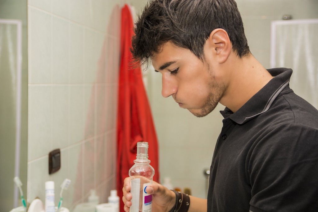 Head and Shoulders Close Up of Attractive Young Man with Dark Hair Rinsing with Mouth Wash in Bathroom as part of Morning Grooming Routine