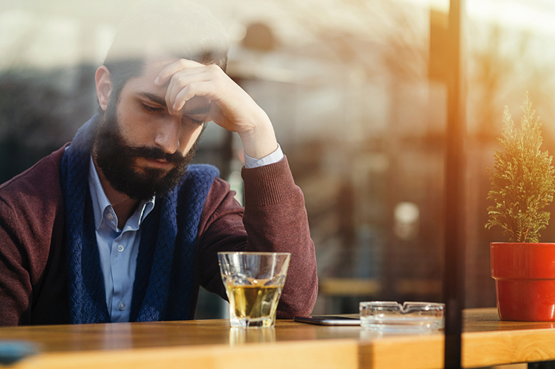 Depressed male drinking alcohol in a bar during daytime