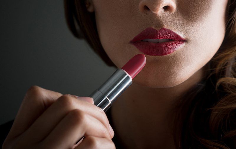 Close-up on  a woman applying red lipstick on her lips straight from the bullet - makeup concepts