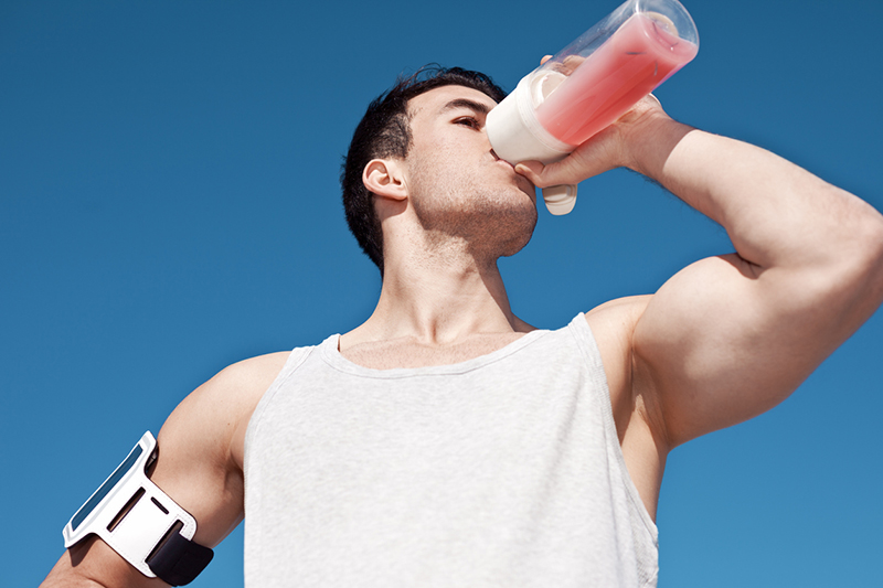 Young and strong athlete drinking protein cocktail on blue sky background
