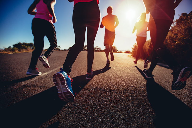 Unusual low angle back view of a group of friends jogging outdoors on a summer afternoon with sun flare